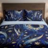Front close view of cobalt bedding with mosaic-like blue leaves, sweeping golden crescents, pale stars and a large circular celestial motif on the cover and matching pillows.