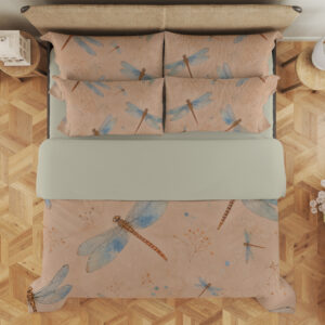 Overhead view of peach bedding printed with blue-winged dragonflies with copper-brown bodies and fine scattered speckles, with the design repeated on the pillows.