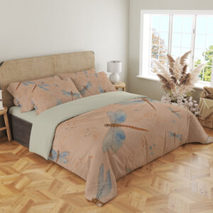 Angled full-bed view of peach bedding printed with blue-winged dragonflies with copper-brown bodies and fine scattered speckles, showing the pattern across the cover and pillows.