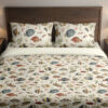 Front close view of ivory bedding with small watercolor reef fish in blue, yellow, coral and gray swimming among delicate sea plants on the cover and matching pillows.
