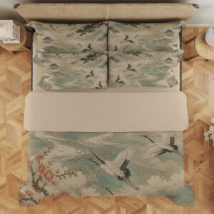Overhead view of bedding printed with white cranes flying over pale teal waves, framed by dark branches and rust-colored blossoms, with the design repeated on the pillows.