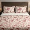Front close view of ivory bedding with a fine garnet-red repeat of roses, small blossoms and curling leafy sprigs on the cover and matching pillows.