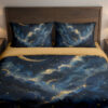 Front close view of navy bedding with billowing blue cloud bands, fine golden edges, small stars and a slender crescent moon on the cover and matching pillows.