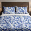 Front close view of ivory bedding with a dense indigo toile-style pattern of peacocks, flowering branches, leafy trees and garden foliage on the cover and matching pillows.
