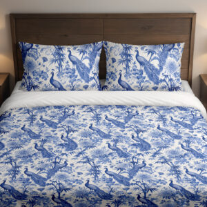 Front close view of ivory bedding with a dense indigo toile-style pattern of peacocks, flowering branches, leafy trees and garden foliage on the cover and matching pillows.
