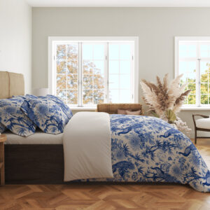 Side view of ivory bedding with a dense indigo toile-style pattern of peacocks, flowering branches, leafy trees and garden foliage, showing the print across the draped cover.