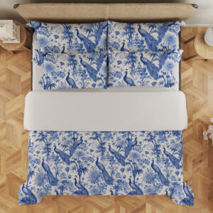 Overhead view of ivory bedding with a dense indigo toile-style pattern of peacocks, flowering branches, leafy trees and garden foliage, with the design repeated on the pillows.