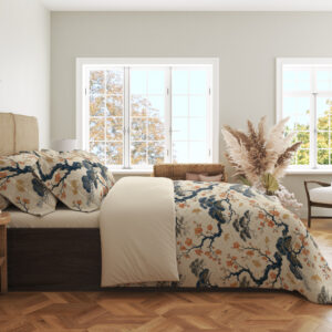 Side view of cream bedding printed with twisting indigo branches, soft blue foliage and clusters of small coral blossoms, showing the print across the draped cover.