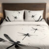 Front close view of ivory bedding printed with large black and gray dragonflies, fine curving lines and scattered ink-like dots on the cover and matching pillows.