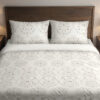 Front close view of ivory bedding with pale-gray floral medallions, tiny dotted flowers and fine scalloped lace-like printed borders on the cover and matching pillows.