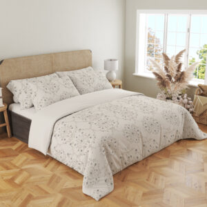 Angled full-bed view of ivory bedding with pale-gray floral medallions, tiny dotted flowers and fine scalloped lace-like printed borders, showing the pattern across the cover and pillows.