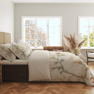 Side view of ivory bedding printed with fine magnolia branches, cream flowers, muted green leaves and a faint gold-colored lattice, showing the print across the draped cover.
