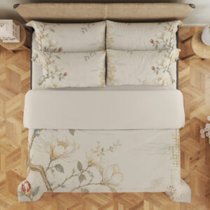 Overhead view of ivory bedding printed with fine magnolia branches, cream flowers, muted green leaves and a faint gold-colored lattice, with the design repeated on the pillows.