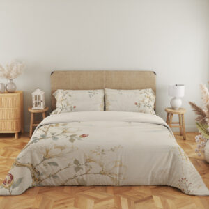 Full front view of ivory bedding printed with fine magnolia branches, cream flowers, muted green leaves and a faint gold-colored lattice beneath a beige headboard.