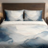 Front close view of bedding printed with layered misty blue and gray watercolor contours, fine pale lines and an open ivory center on the cover and matching pillows.