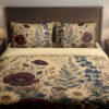 Front close view of parchment-cream bedding with burgundy poppies, ivory daisies, tall indigo flowers and fine fern fronds on the cover and matching pillows.