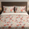 Front close view of ivory bedding with a dense delicate repeat of coral-pink roses, burgundy leaves, pale teal foliage and tiny peach blossoms on the cover and matching pillows.