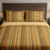 Front close view of bedding with narrow vertical saffron, cream, orange and olive stripes filled with tiny folk flowers, leaf stems and dotted borders on the cover and matching pillows.