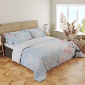 Angled full-bed view of pale blue bedding printed with delicate pink blossoms on dark branches and scattered petals around an open misty center, showing the pattern across the cover and pillows.