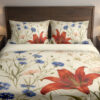 Front close view of cream bedding printed with large red lilies, blue cornflowers and fine green meadow stems on the cover and matching pillows.