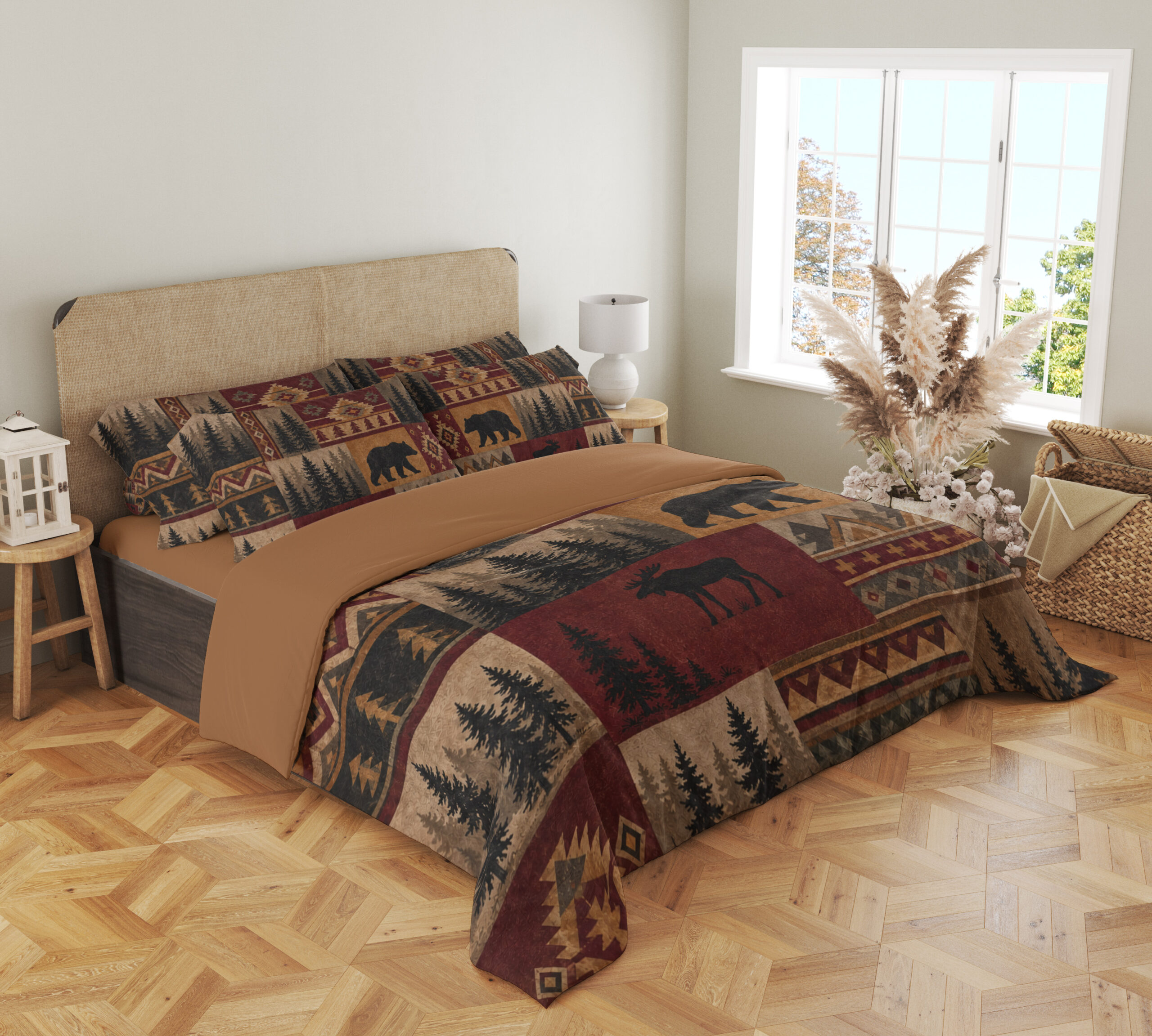 Angled full-bed view of bedding printed with burgundy, ochre and tan patchwork panels of black bears, moose, pine trees and geometric borders, showing the pattern across the cover and pillows.