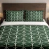 Forest-green bedding with ivory looping leaves running down the duvet and matching pillows, shown close up from the foot of the bed.