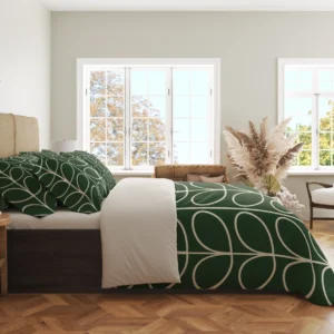Side view of the green duvet with large ivory leaf loops curving over its hanging edge beside a plain pale fold and patterned pillows.