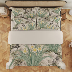 Overhead view of ivory bedding printed with white and yellow narcissus flowers, long sage leaves and dark mossy rock formations, with the design repeated on the pillows.