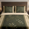 Front close view of olive bedding printed with pale botanical sprigs and tiny star-like marks, framed by cream borders with small leaf motifs on the cover and matching pillows.