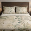 Front close view of parchment bedding printed with sage fern fronds, round eucalyptus-like leaves, delicate grasses and small moth motifs on the cover and matching pillows.