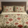 Front close view of cream bedding printed with scarlet drooping bell-shaped flowers, small yellow berries and curling olive-green vines on the cover and matching pillows.