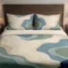 Front view of cream, blue-gray and sage contour fields with faint curved lines on a duvet cover and matching pillowcases against a dark wooden headboard.