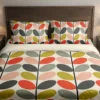 Cream bedding with mustard, peach, red-orange, sage-gray and charcoal oval leaves on dark stems across the duvet and pillows, viewed closely from the front.
