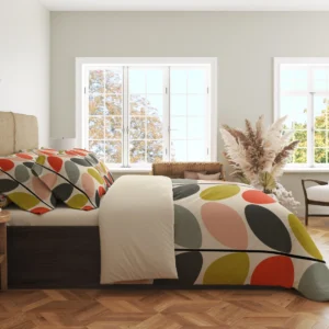 Side view of cream bedding with multicolor oval leaves draped over the duvet edge, including peach and charcoal leaves beside a plain cream fold.