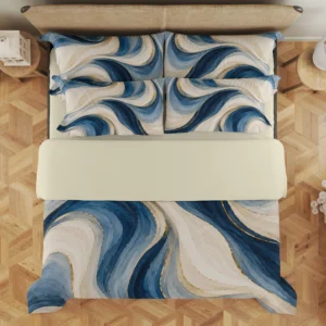 Overhead view of ivory and blue flowing ribbons with gold-colored accents on the duvet cover and styled matching pillows, with a pale cream fold across the bed.