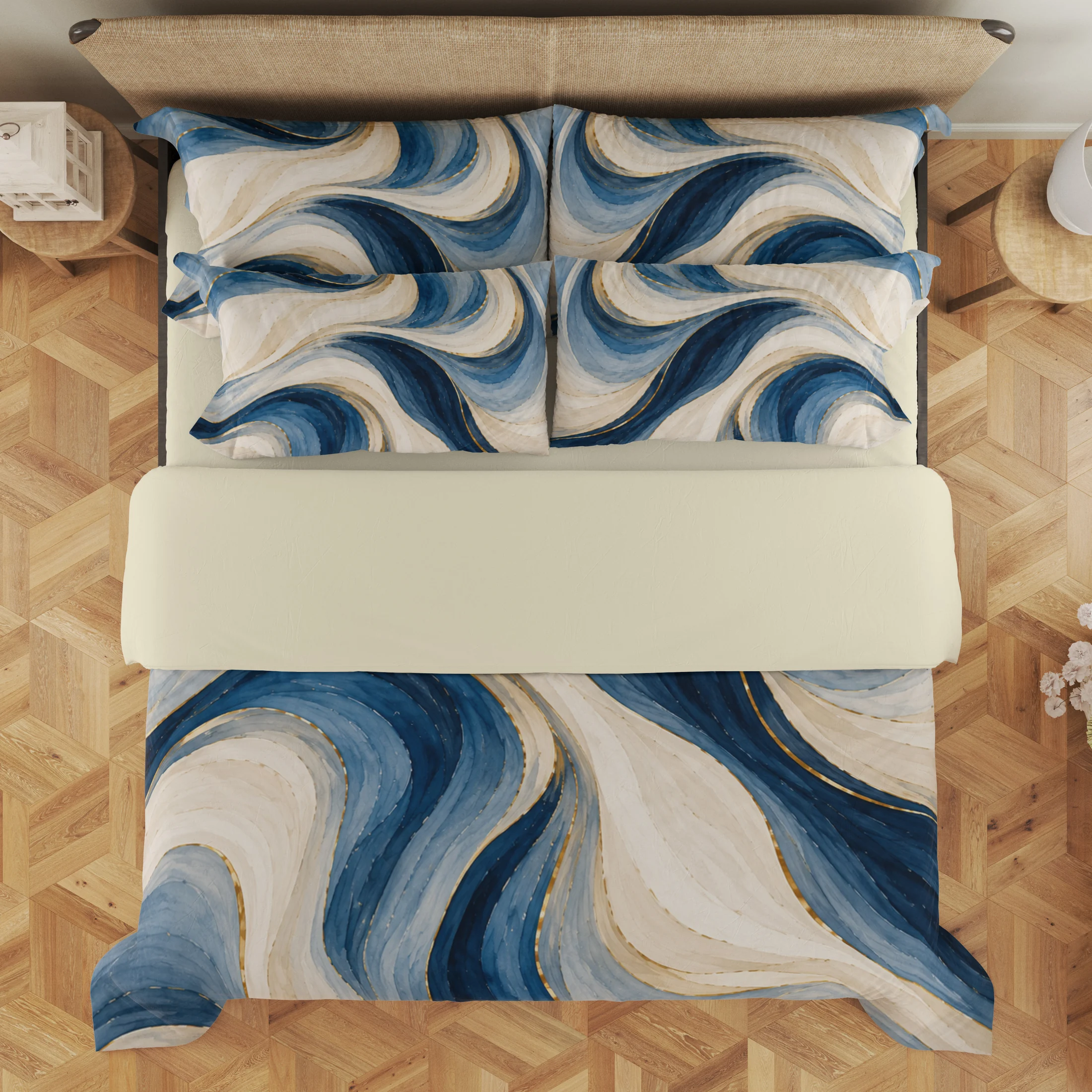 Overhead view of ivory and blue flowing ribbons with gold-colored accents on the duvet cover and styled matching pillows, with a pale cream fold across the bed.
