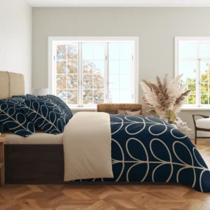 Side view of navy bedding showing cream looped leaves over the hanging duvet edge and smaller loops on the pillows beside a pale fold.