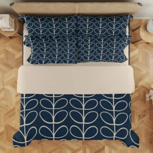 Navy duvet and layered pillows seen from above, with cream leaf stems visible below a broad plain cream folded section.