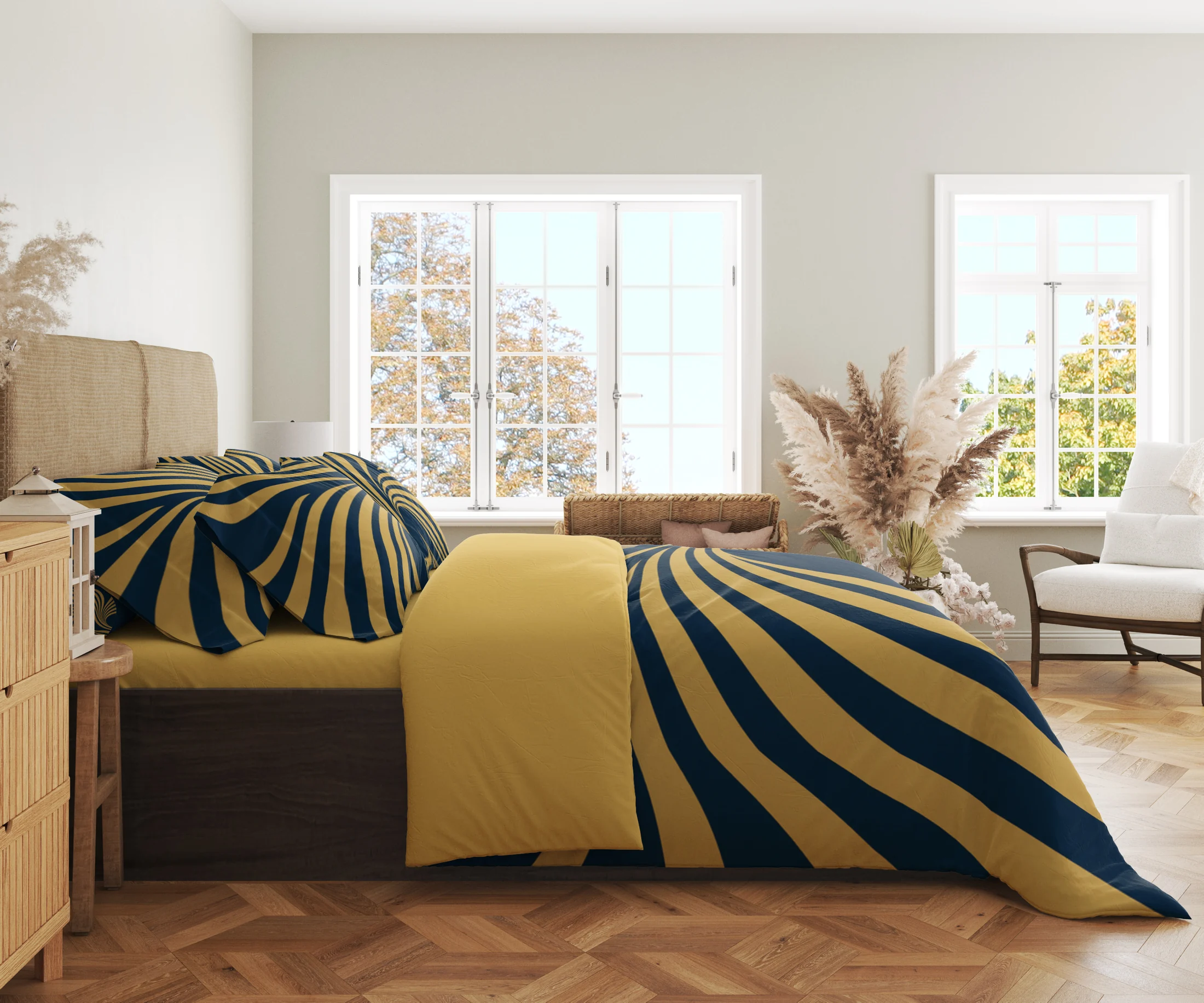 Side view of navy bedding crossed by broad gold-colored ribbons, with printed pillows and a gold-colored fold in a bright windowed room.