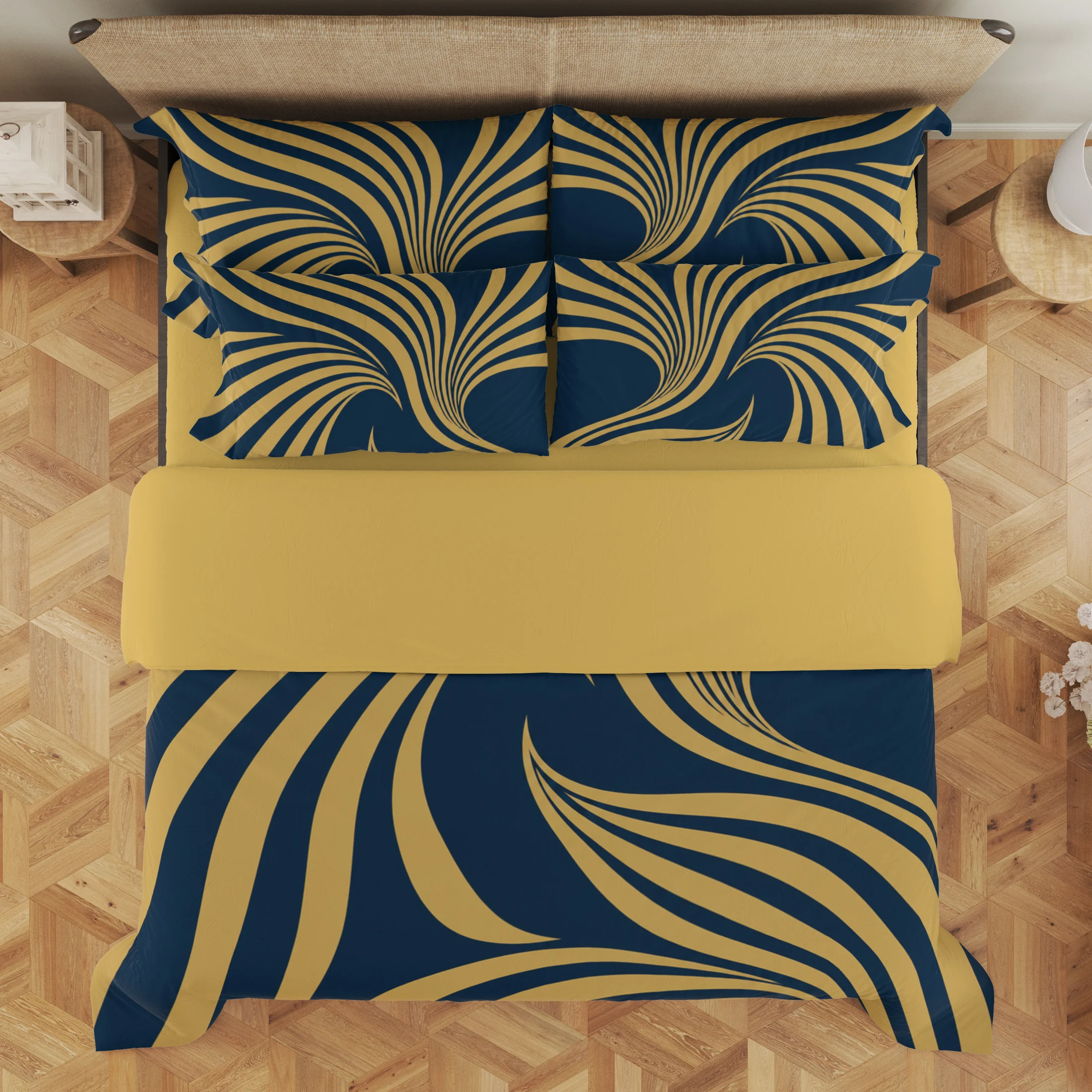 Overhead view of navy and gold-colored ribbon-fan bedding with a wide gold-colored fold and four styled printed pillows on a wood floor.