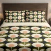 Charcoal bedding with cream flowers, peach centers and olive leaf medallions across the duvet and pillows, shown close up from the front.