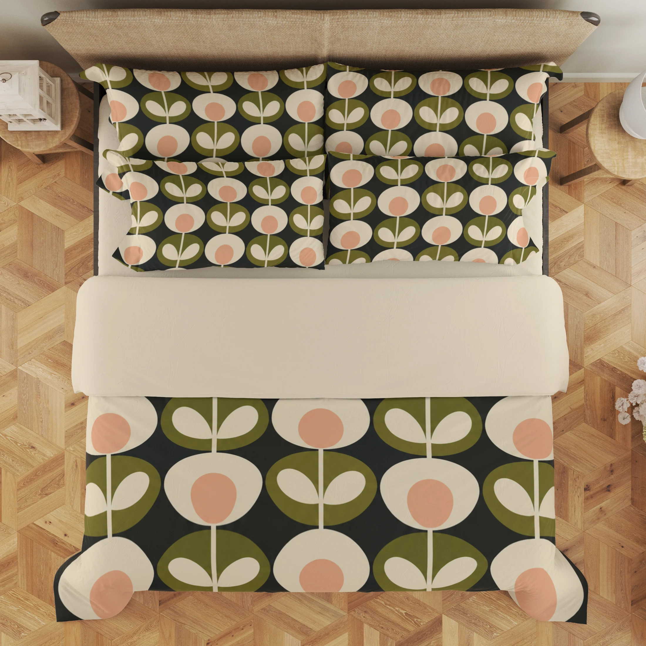 Overhead view of charcoal bedding with alternating cream flowers and olive paired-leaf motifs below a broad cream fold and across layered pillows.