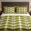 Ivory bedding with broad olive-green leaves and slender charcoal stems running down the duvet and matching pillows, viewed closely from the front.