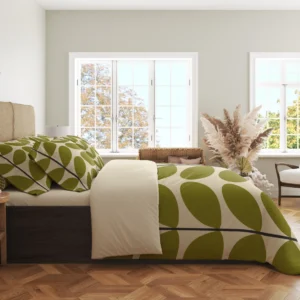Side view of ivory bedding with large olive leaves and a dark stem bending over the hanging duvet edge beside a plain cream fold.