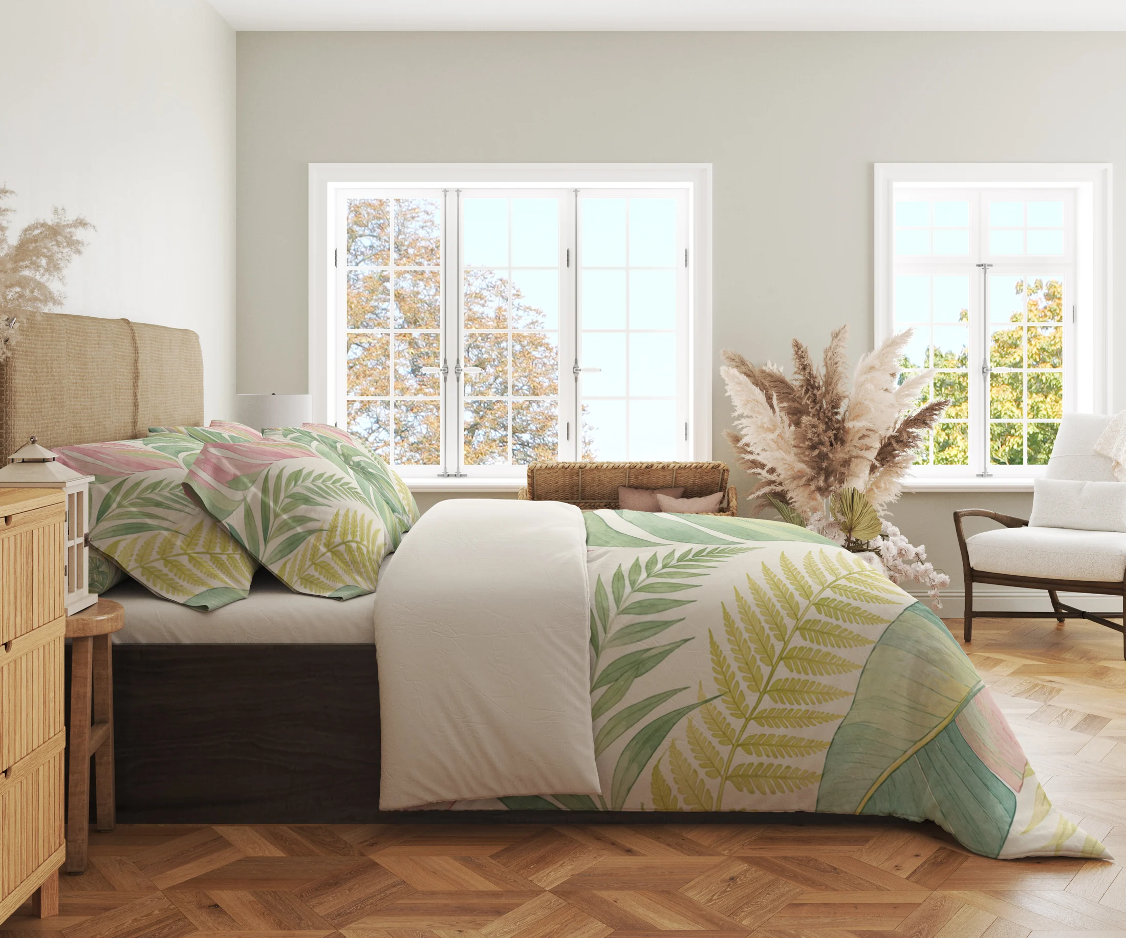 Side view of pastel green tropical leaves, blush foliage and pale yellow fronds on a cream duvet cover and matching pillowcases in a bright windowed room.