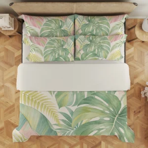 Overhead view of sage and blush split leaves, pale yellow fronds and tropical foliage on the cream duvet cover and styled matching pillows, with a pale fold.