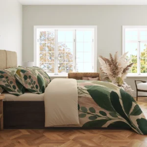 Side view of sage and blush brushstroke bedding with dark green leaf sprays, printed pillows and a cream fold in a bright windowed room.