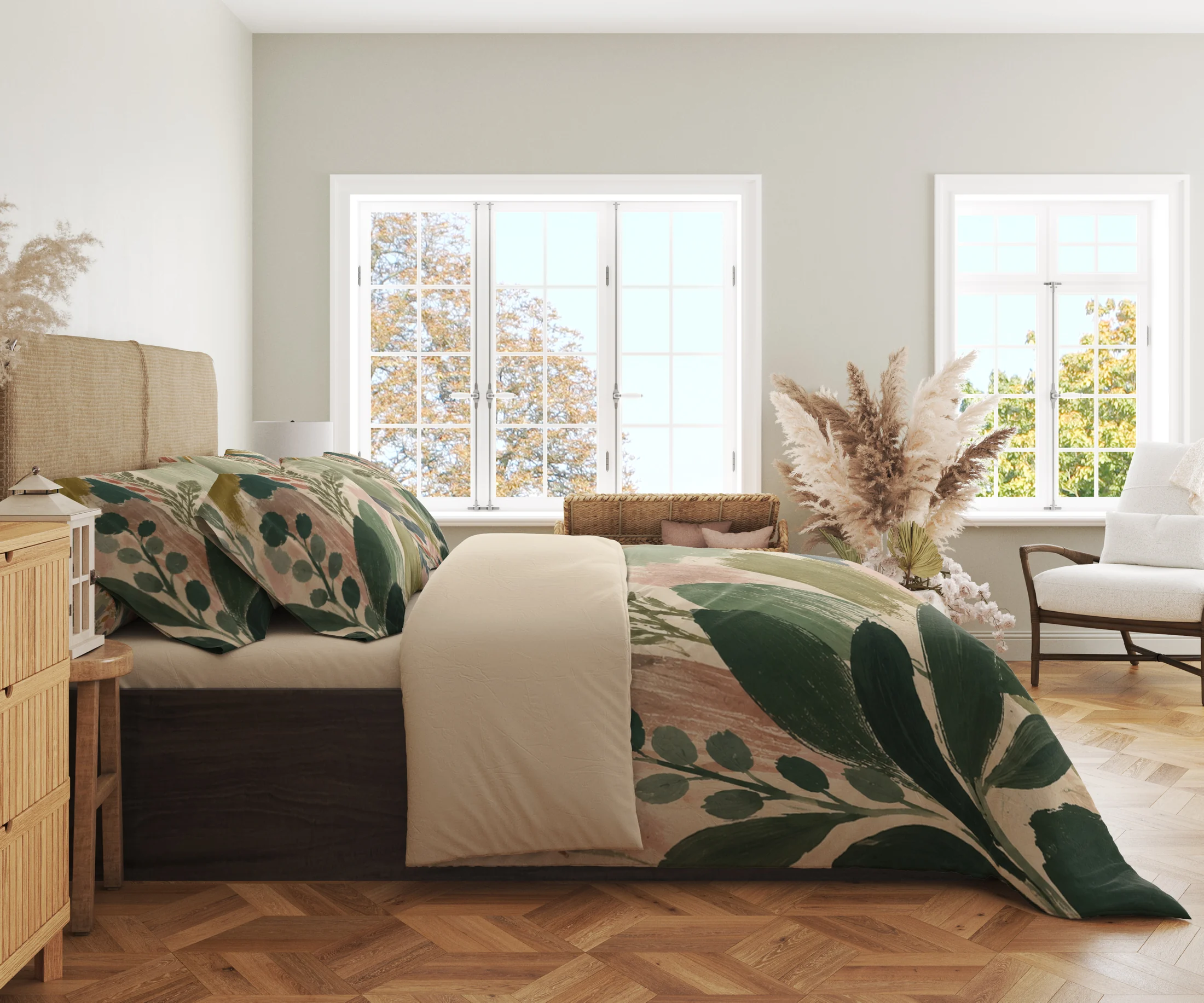 Side view of sage and blush brushstroke bedding with dark green leaf sprays, printed pillows and a cream fold in a bright windowed room.
