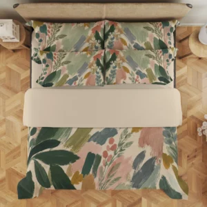 Overhead view of sage and blush botanical brushstroke bedding with a wide cream fold and four styled printed pillows.