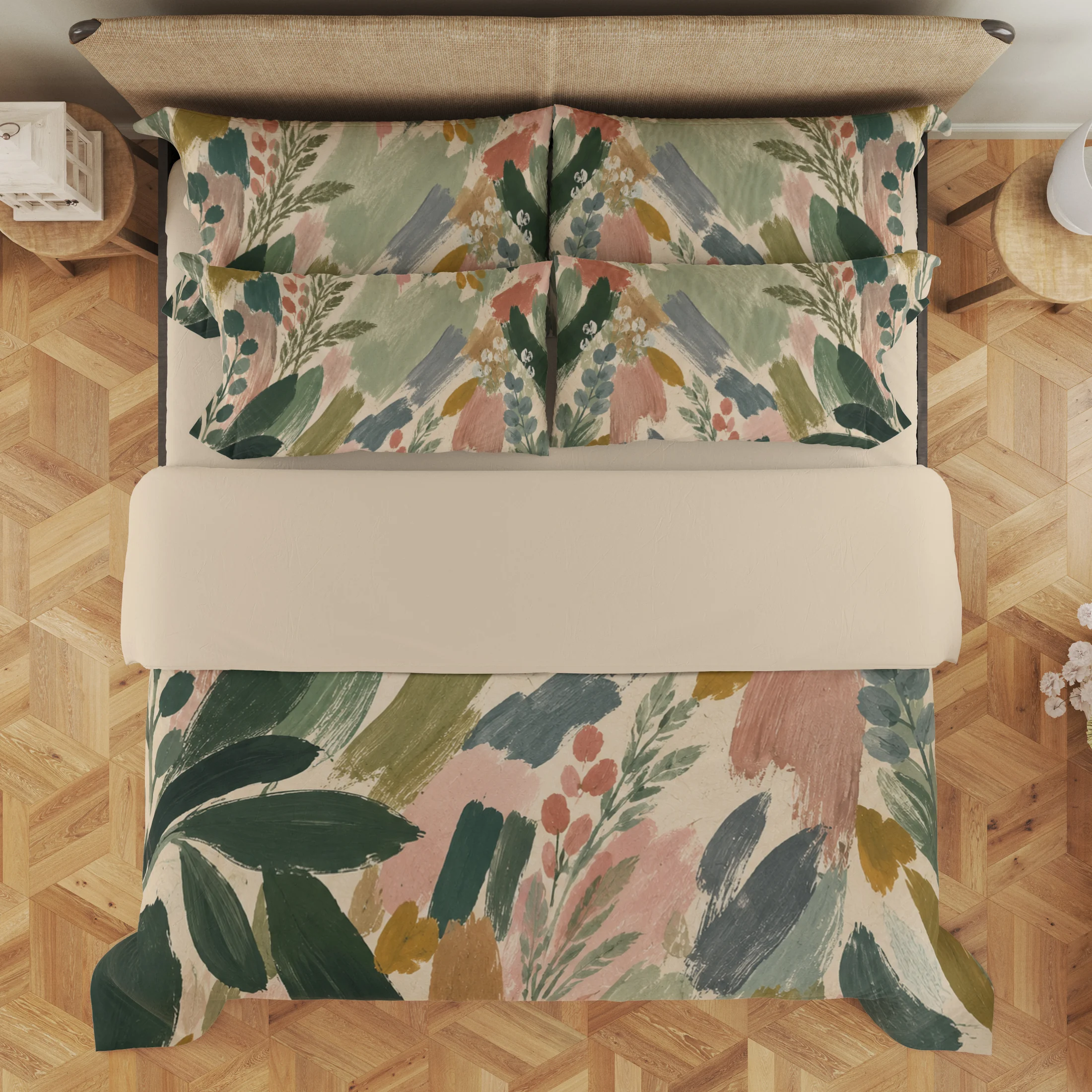 Overhead view of sage and blush botanical brushstroke bedding with a wide cream fold and four styled printed pillows.